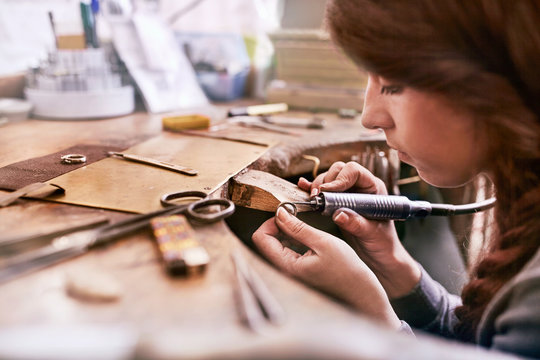 Serious focused female jeweler using equipment in workshop