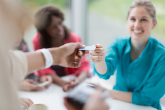 Smiling woman paying waitress with credit card reader at cafe table
