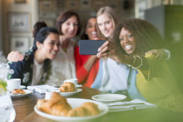 Smiling women friends taking selfie with camera phone in restaurant