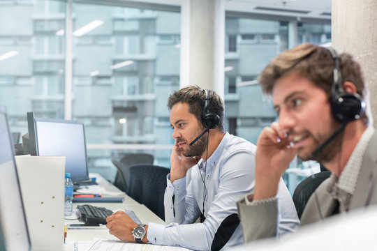 Businessmen handsfree devices talking on telephone working at computers in office
