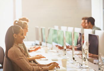 Telemarketers wearing headsets working at computers in a row in sunny office