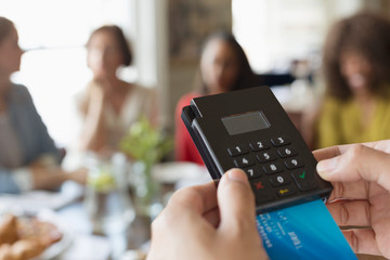 Close up waitress using credit card reader at cafe table