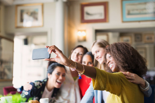 Smiling women friends taking selfie with camera phone in restaurant