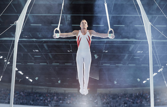 Male gymnast balancing arms outstretched on gymnastics rings in arena