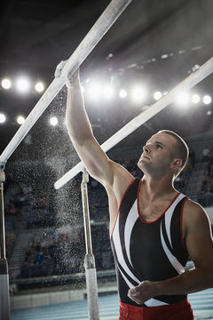 Male gymnast applying chalk powder to parallel bars in arena