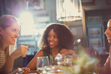Smiling women friends dining and talking at restaurant table