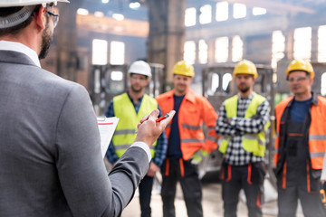 Steel workers listening to manager in meeting in factory