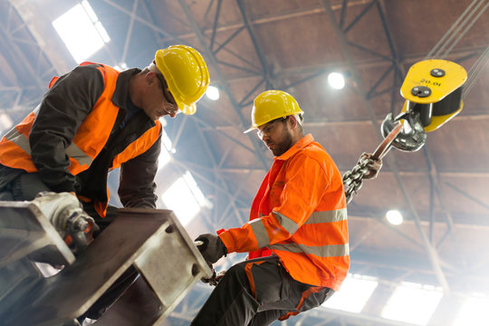 Steel workers fastening crane hook to steel in factory