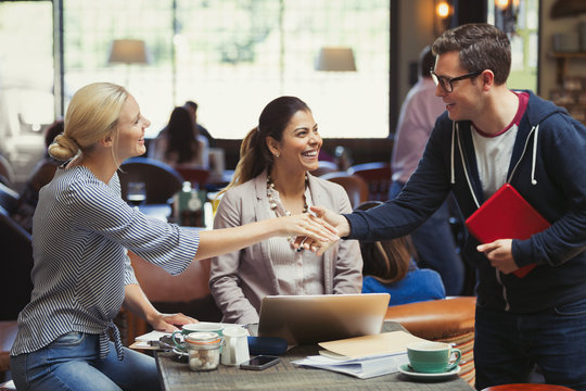Creative business people greeting, handshaking at cafe