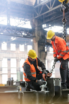 Steel workers fastening crane chain to steel in factory