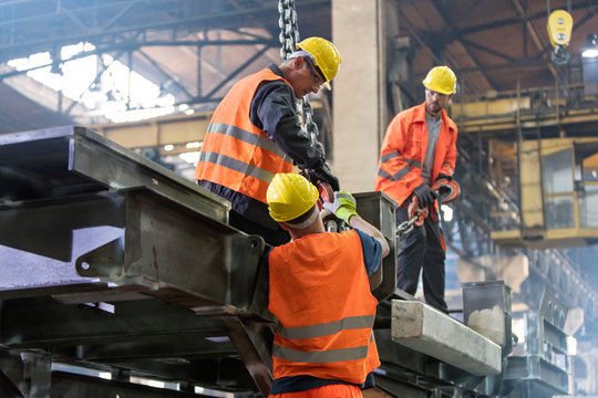 Steel workers fastening crane hook to steel in worker