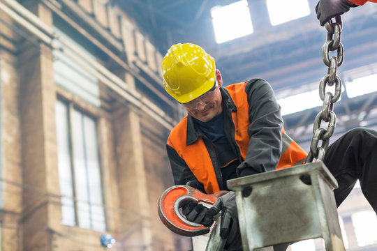 Steel worker fastening crane chain to steel in factory
