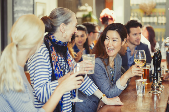 Smiling women friends drinking wine at bar