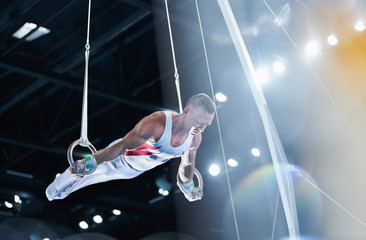 Male gymnast performing on gymnastics rings in arena