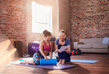 Fitness instructor and young woman using digital tablet in gym studio