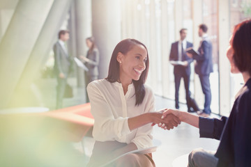 Smiling businesswomen handshaking in office lobby