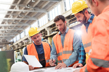 Steel workers and engineers meeting reviewing blueprints in factory