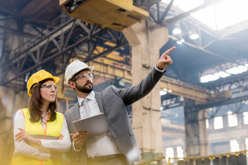 Manager and female steel worker talking looking away in factory