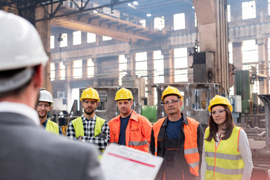 Steel workers listening to manager in meeting in factory