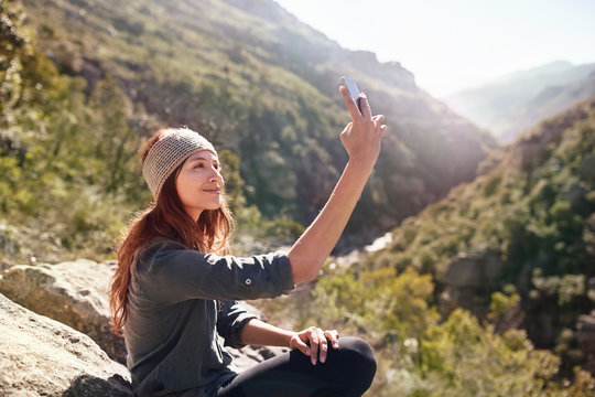 Young woman taking selfie with camera phone on sunny, remote rock
