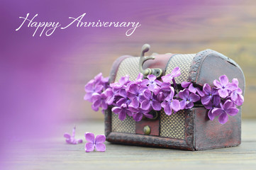 Obraz na płótnie Canvas Anniversary card with violet lilac flowers in wooden chest
