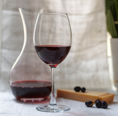 Glass of red wine and carafe with wine, cheese and grapes on a light background
