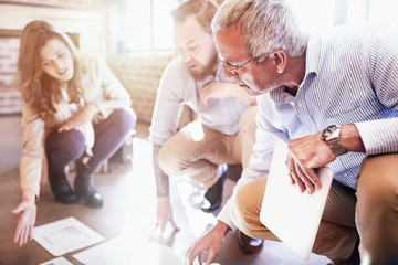 Business people reviewing discussing paperwork on sunny office floor