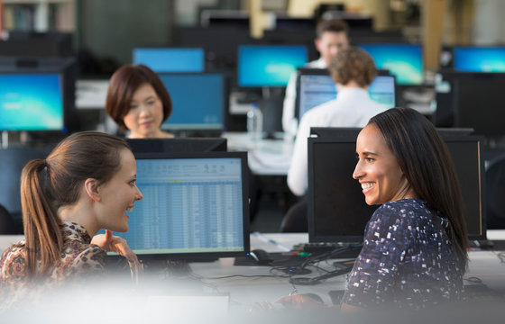 Smiling businesswomen talking at computers in open plan office