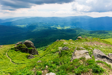 mountain landscape in summer. view from the top of carpathian watershed ridge in to the distance. boulders on the green grassy slopes. sunny weather with clouds on the blue sky