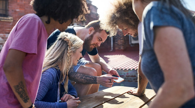 Man showing smart phone to friends at sunny picnic table