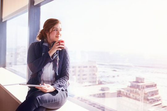 Pensive businesswoman digital tablet drinking coffee at sunny urban window