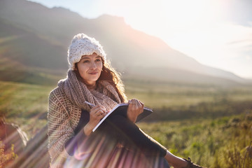 Young woman writing in journal in sunny, remote field