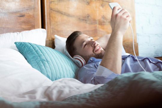 Man listening to music with headphones and mp3 player laying on bed