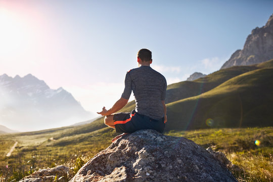 Young man meditating on rock in sunny, remote valley