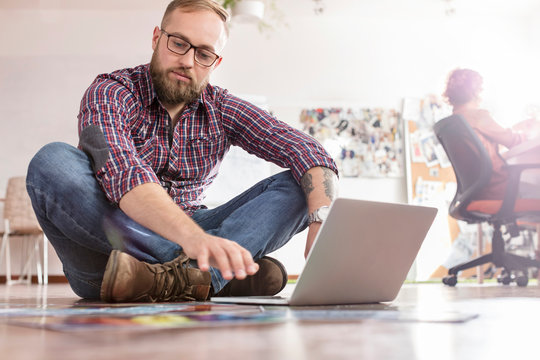 Male design professional reviewing proofs at laptop on office floor