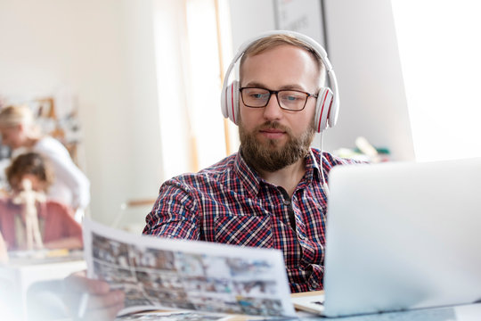 Design professional listening to music headphones reviewing proofs at laptop