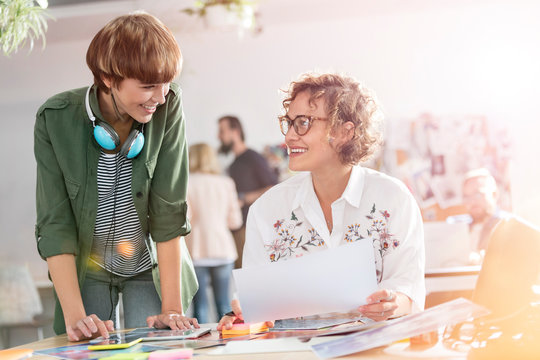 Smiling female design professionals reviewing proofs in office