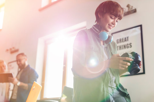 Female design professional with headphones using SLR camera in office