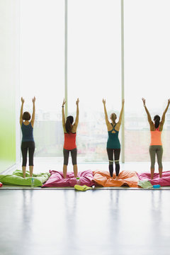 Women on cushions stretching arms raised in exercise class gym studio