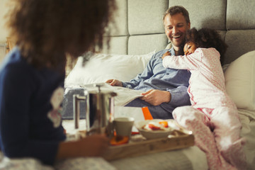 Multi-ethnic daughter hugging father reading newspaper on bed