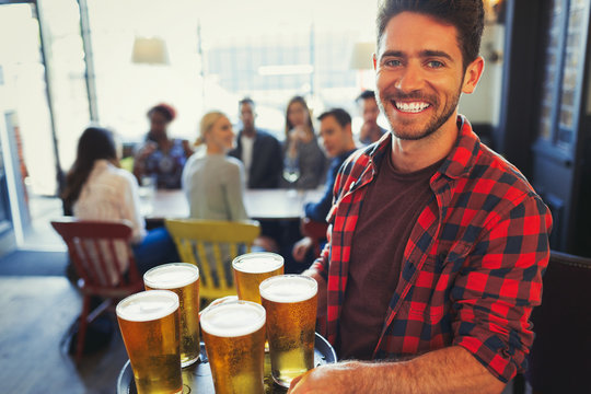 Portrait smiling bartender carrying tray of beer glasses in bar