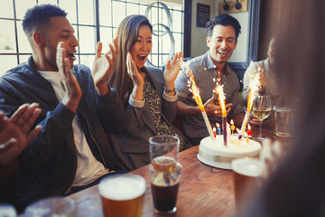 Friends cheering for woman celebrating birthday fireworks cake at table in bar
