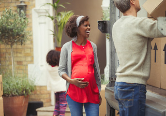 Multi-ethnic pregnant couple unpacking moving van outside new house