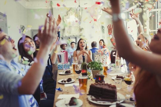 Friends celebrating birthday throwing confetti overhead at restaurant table