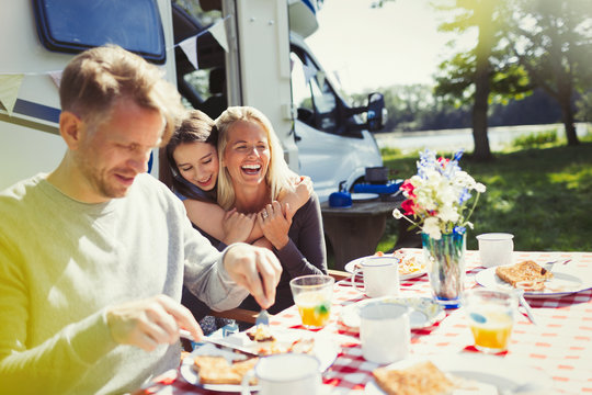 Happy family hugging and eating breakfast outside sunny motor home