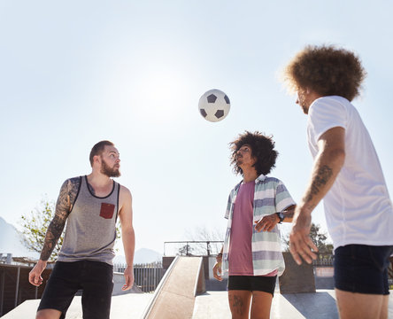 Male friends playing soccer at sunny skate park
