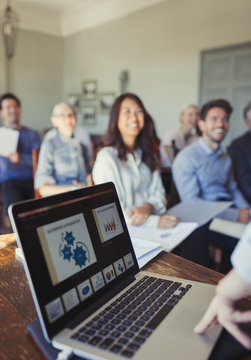 Audience watching businessman at laptop leading conference presentation
