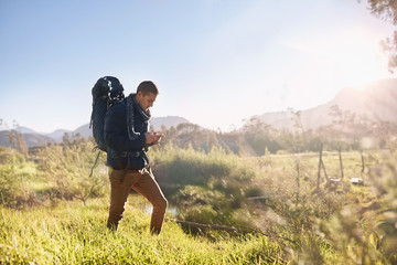 Young man backpack hiking, checking compass in sunny, remote field
