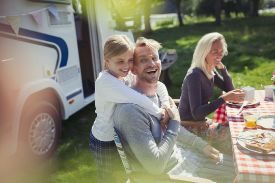 Happy, affectionate father daughter hugging outside sunny motor home