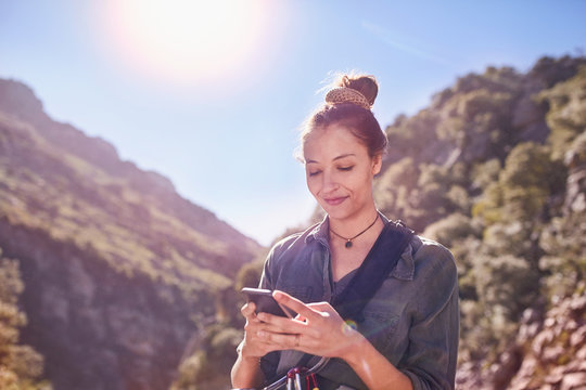 Young woman texting with cell phone below sunny cliffs
